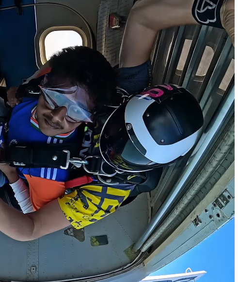 At the plane door — the semi-open hatch, the harness on, the goggle cover over the glasses. This is where the wait ends.